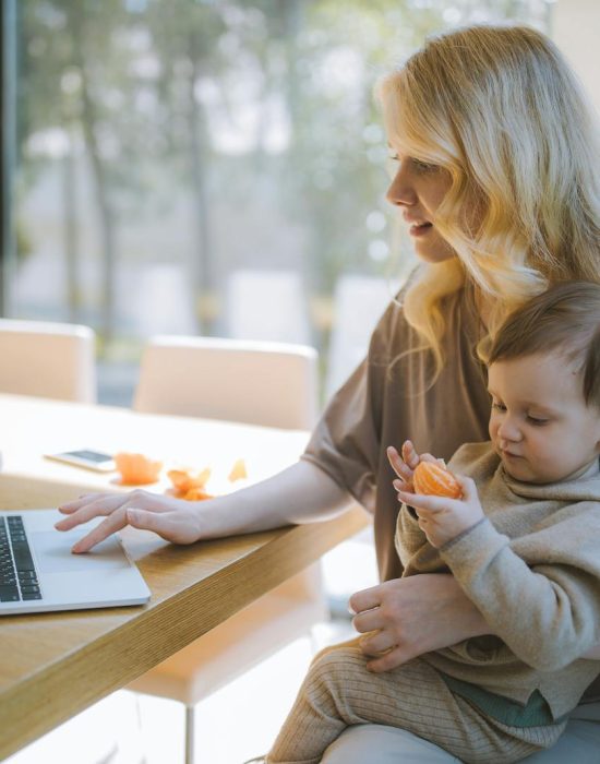 Woman Carrying her Baby and Working on a Laptop